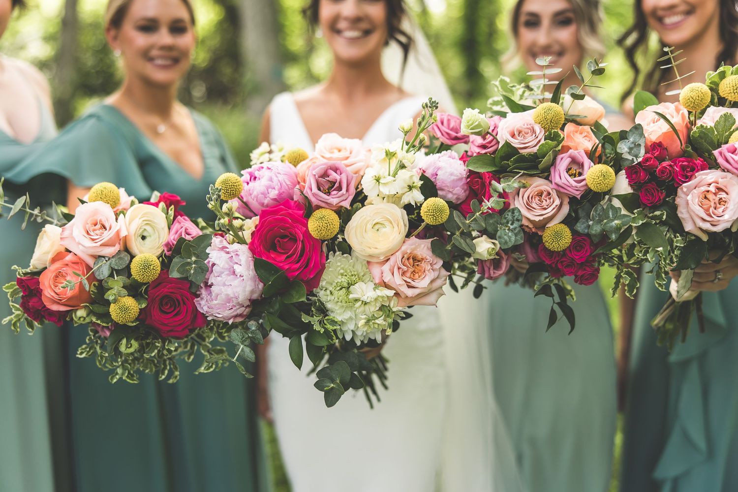 Stunning floral arrangement of pink and peach roses with greenery against sage green dresses.