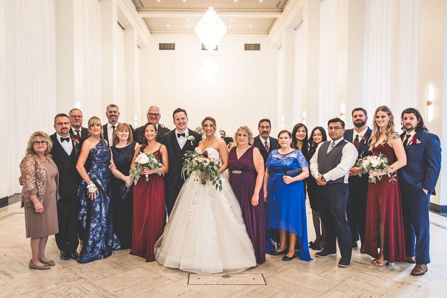 Large wedding party group photo in formal attire standing together in an elegant venue.