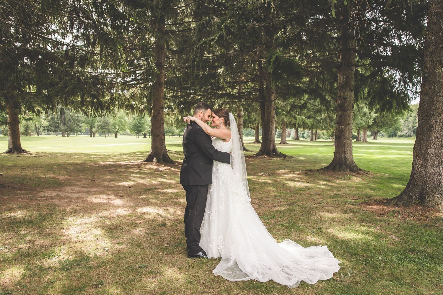 Romantic wedding couple photos taken under tall evergreen trees in a park.