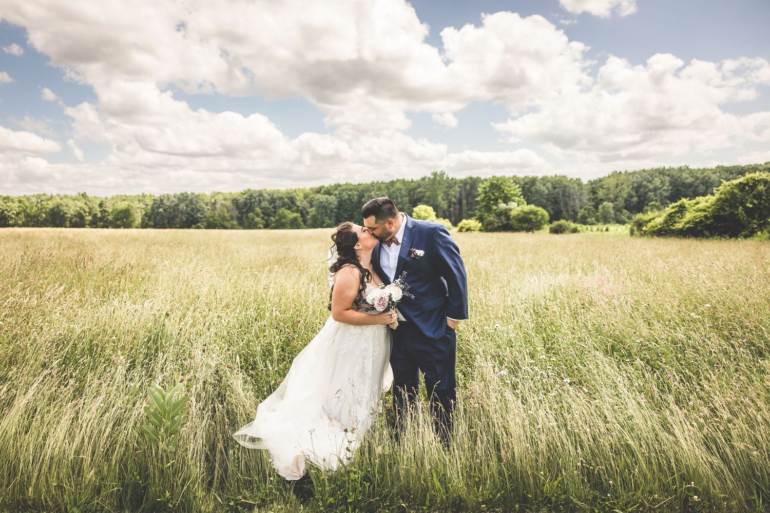 Romantic wedding couple portraits in tall grass field under blue summer sky.