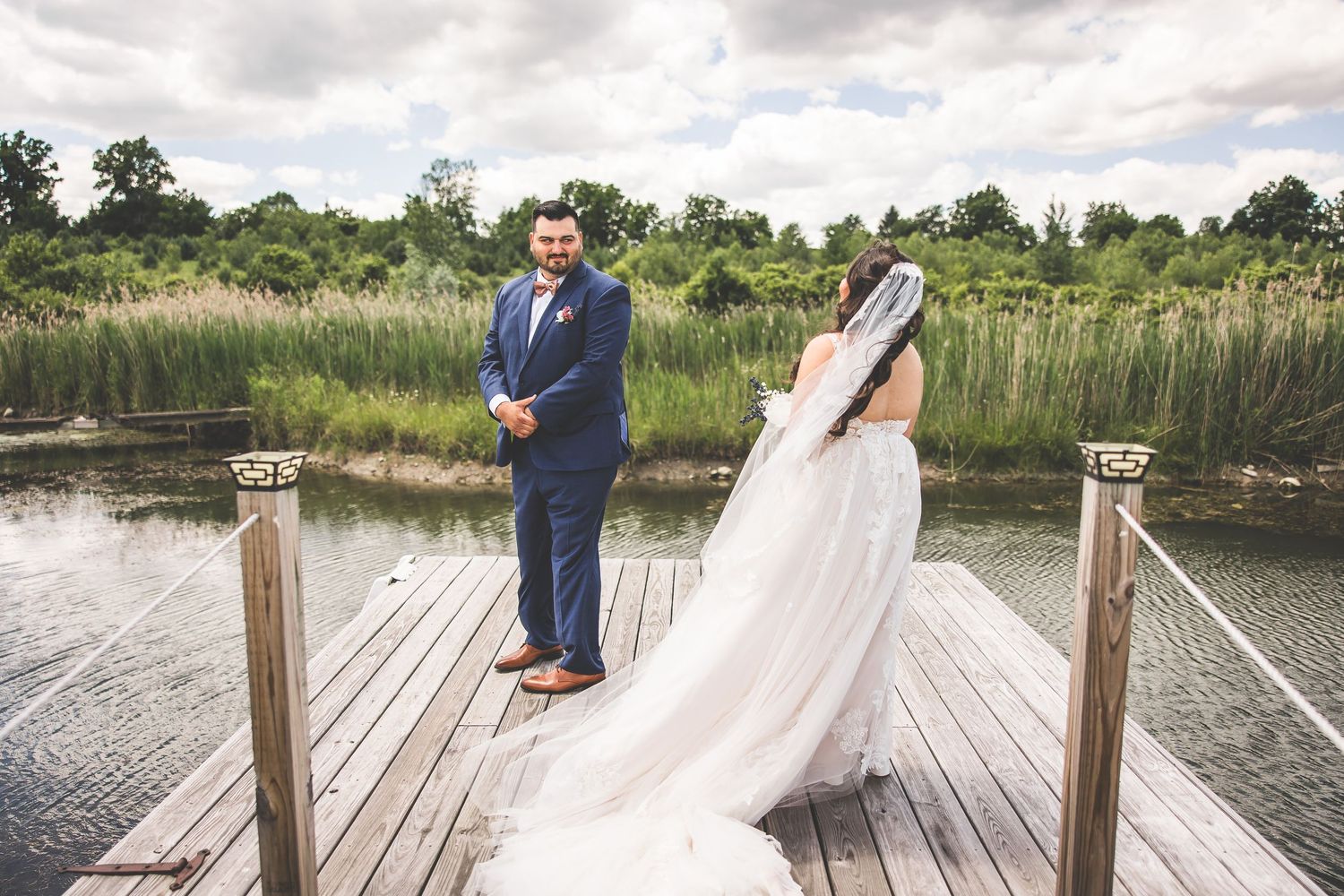 Romantic wedding photos captured on a lakeside wooden dock under cloudy skies.