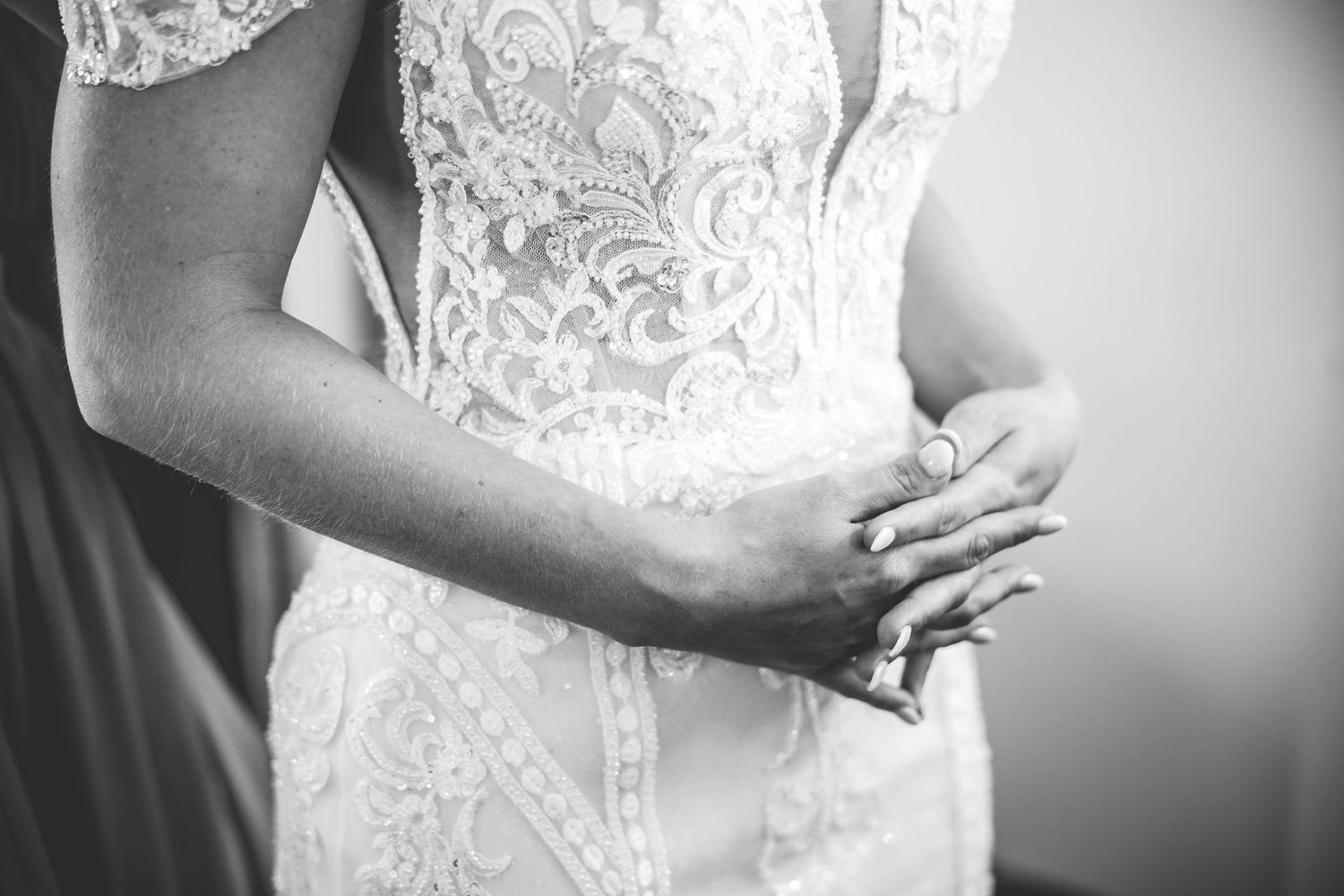Close-up detail of intricate white lace wedding dress bodice with hands clasped.