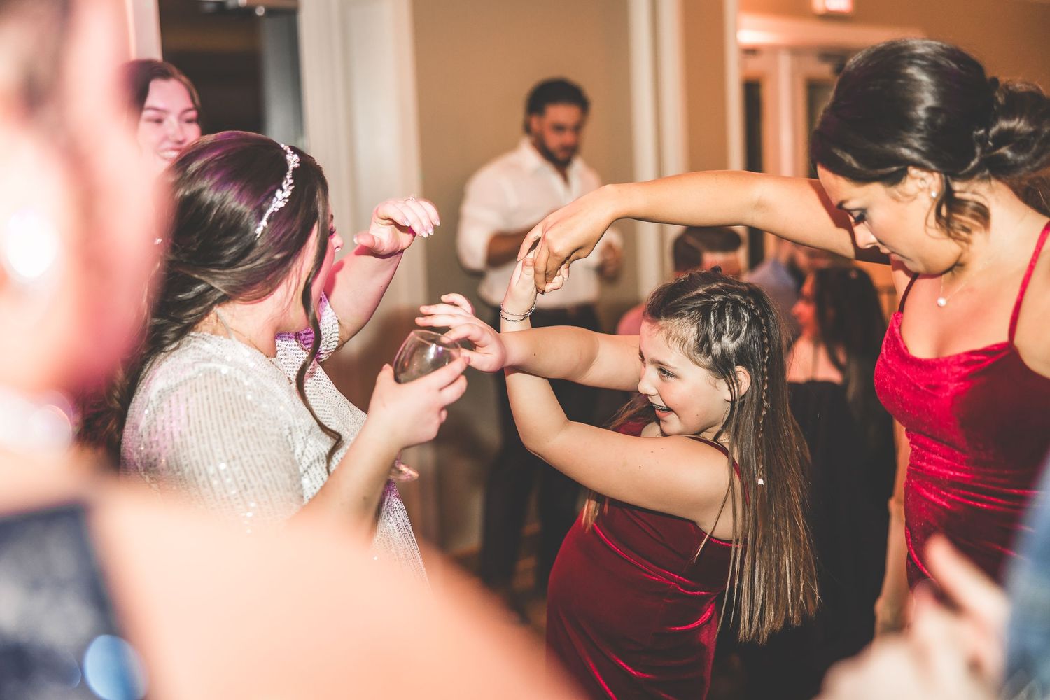 Wedding guests dancing and celebrating at reception with warm ambient lighting.