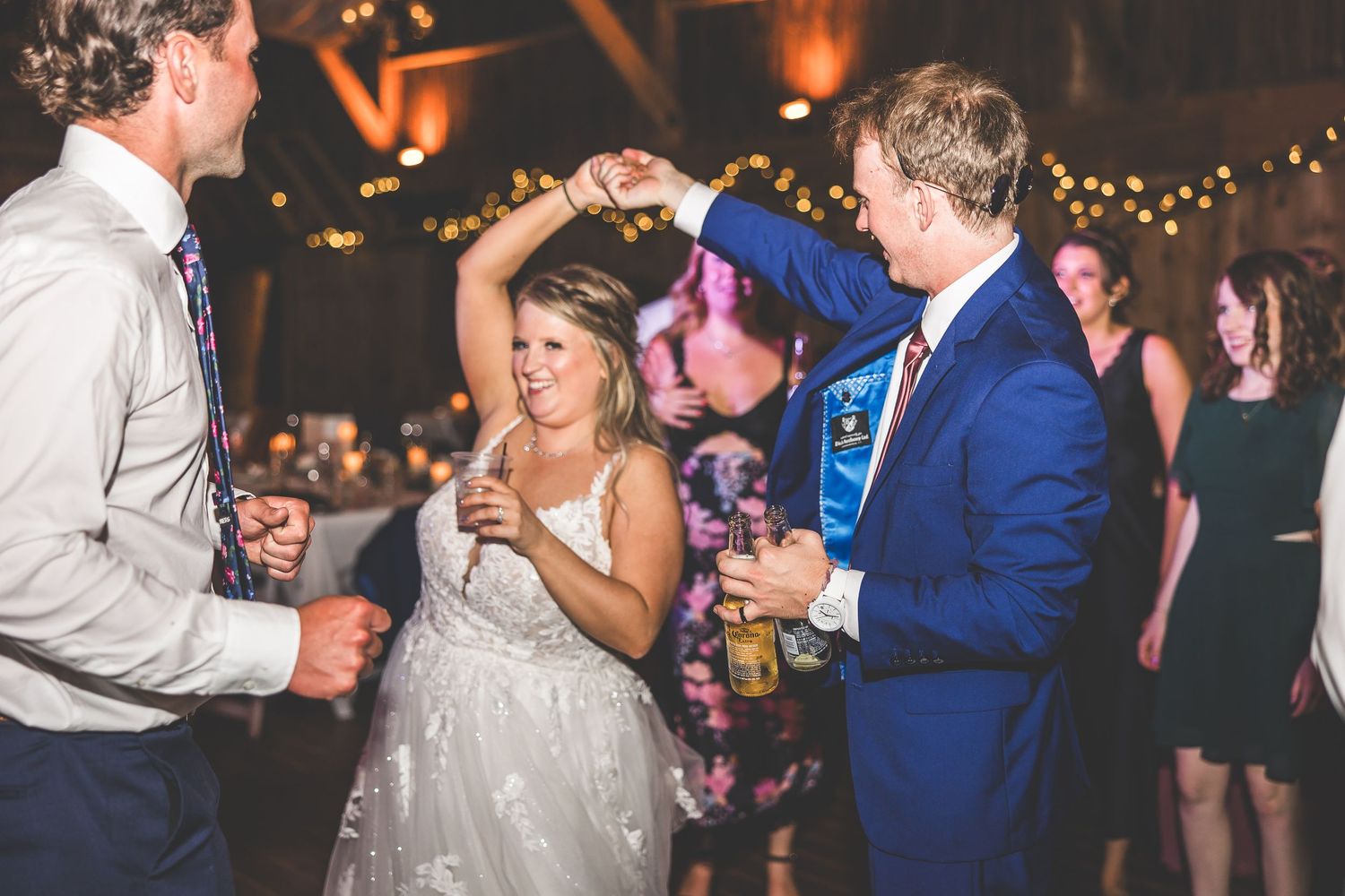 Wedding celebration with guests dancing and socializing under string lights in an indoor venue.