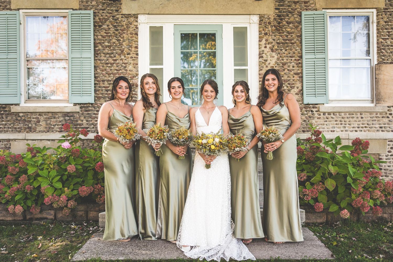 Bridesmaids in champagne dresses pose with the bride in front of a historic stone building.