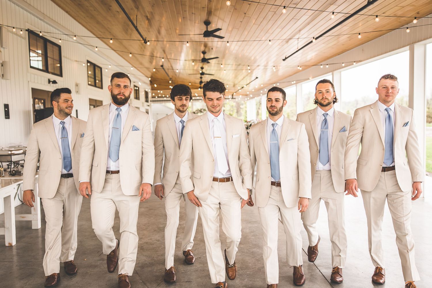 Groomsmen in coordinated cream suits and blue ties pose for formal wedding photo.