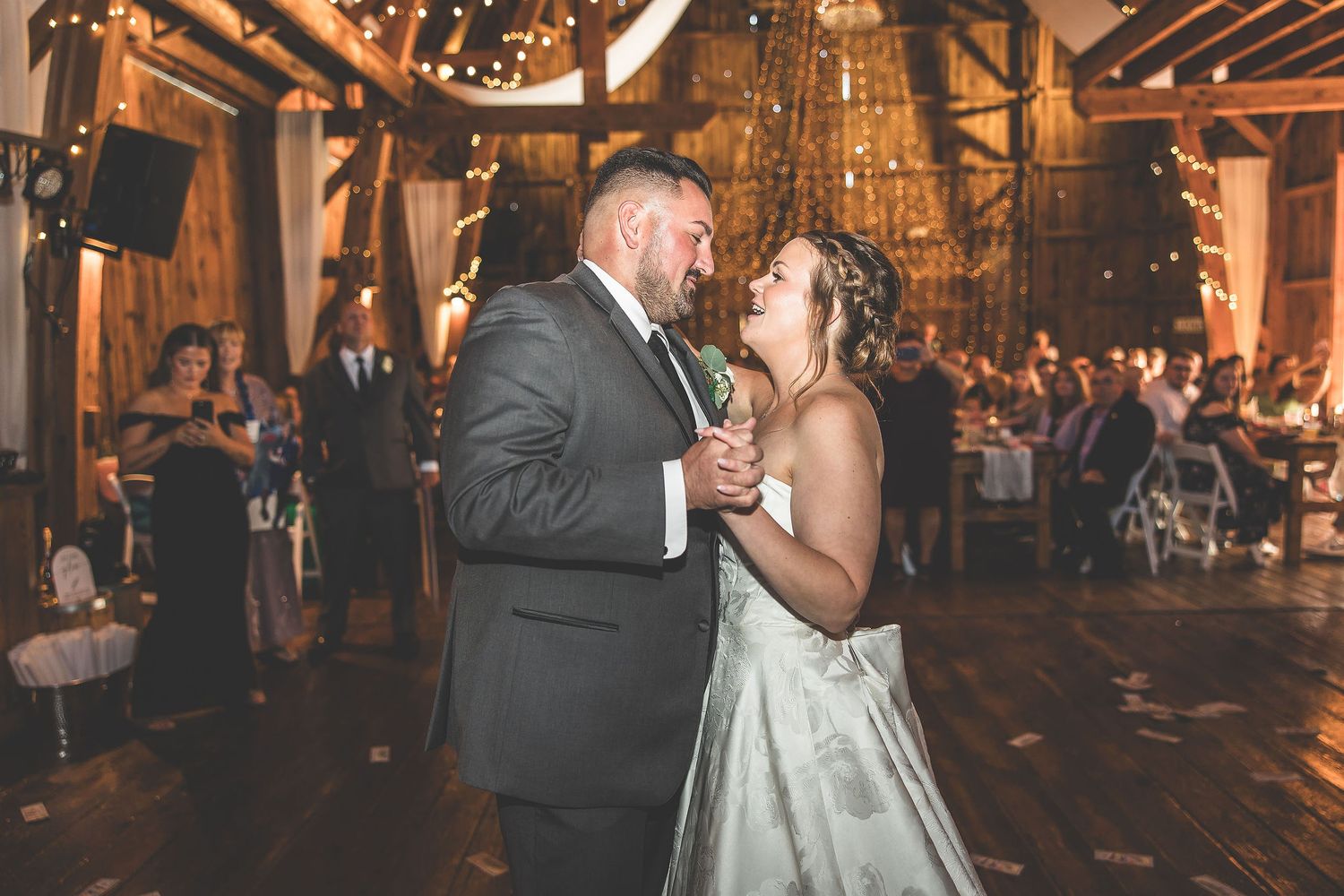 Wedding couples share intimate dances in rustic barn venue with warm ambient lighting.