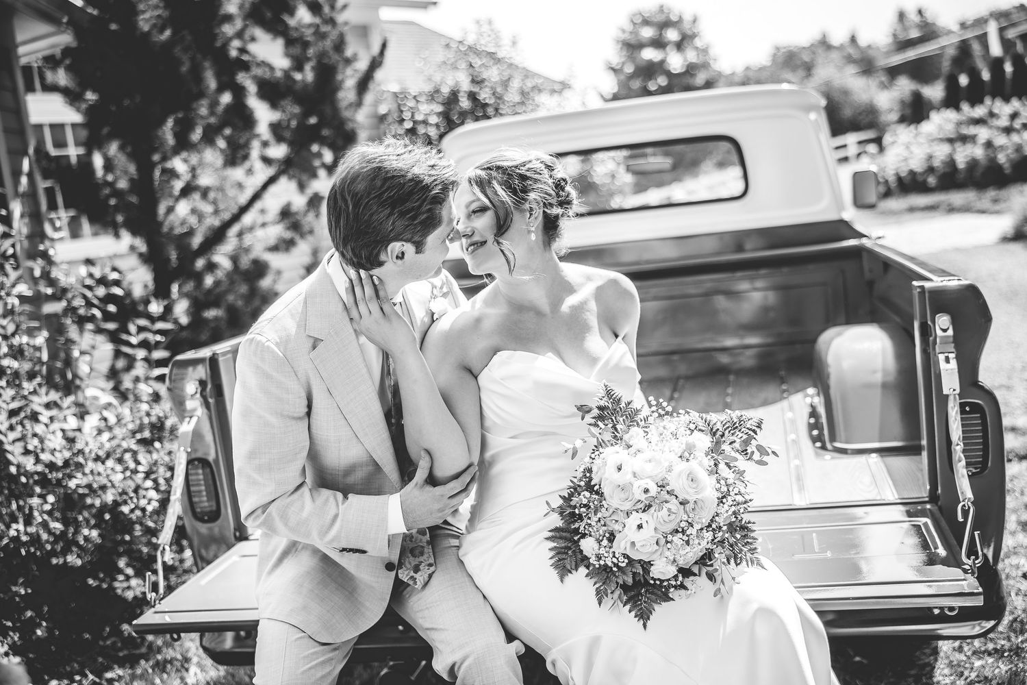 Wedding party poses with a vintage car outdoors on a sunny day.