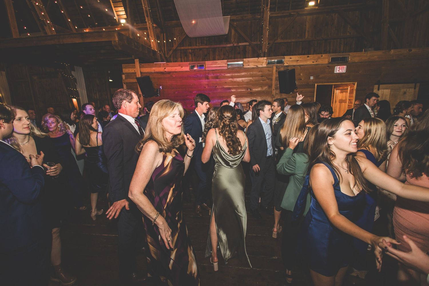 Lively dance floor scene at wedding reception with guests celebrating in rustic venue.