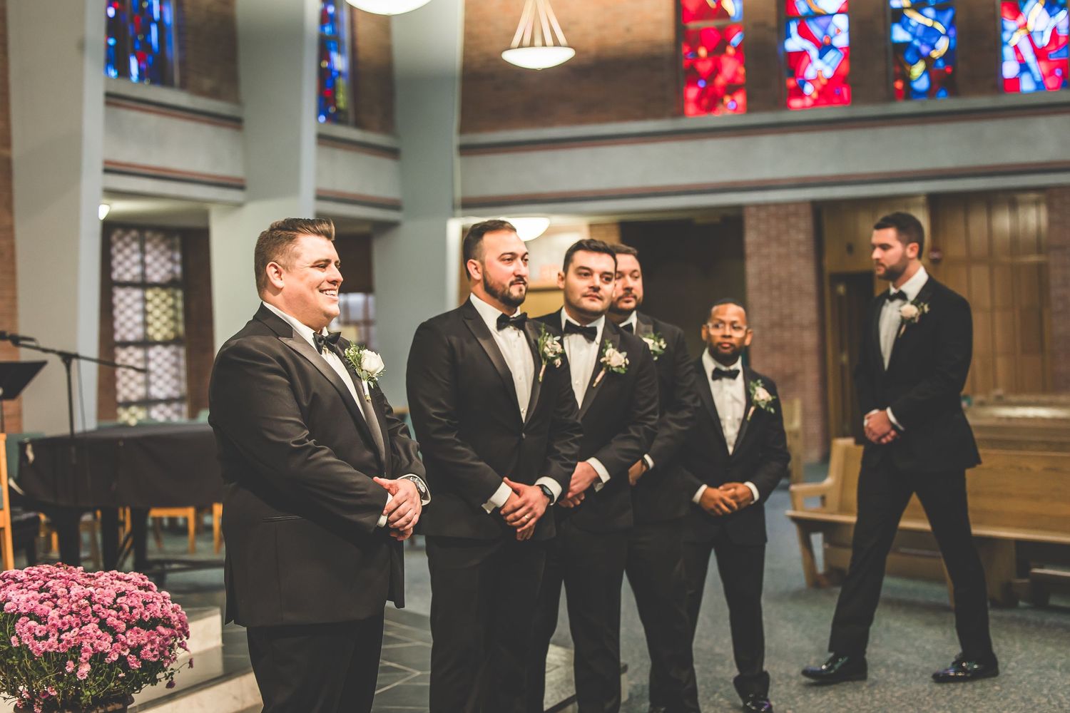 Black and white portrait of a groom in tuxedo with boutonniere smiling at church.