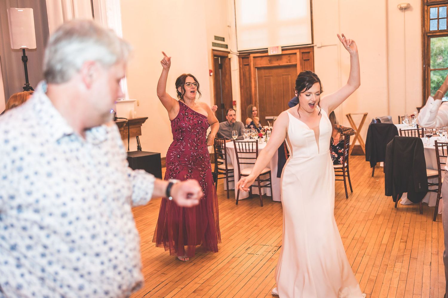 Wedding celebration with guests dancing energetically on a hardwood floor in an elegant venue.