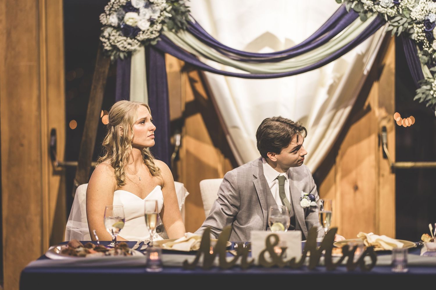 Wedding reception venue decorated with white drapes and floral arrangements in an elegant rustic barn setting.