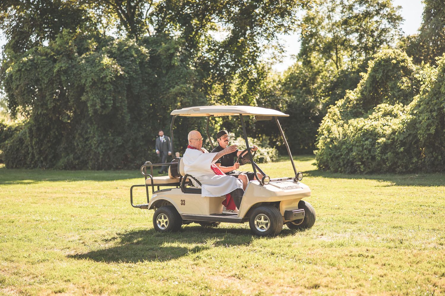 Golf cart driving across a sunny lawn at an outdoor wedding venue.