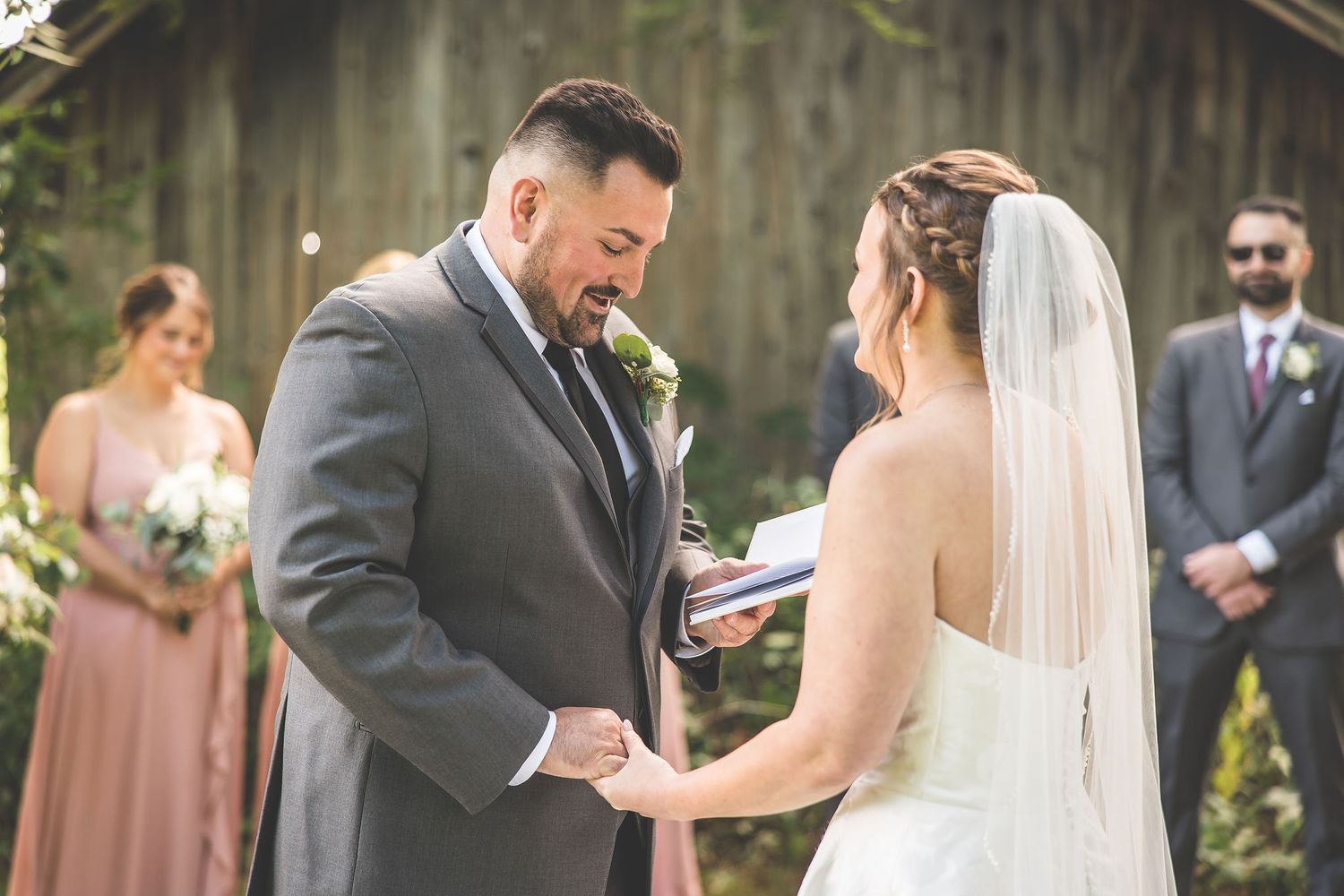 A couple exchanges vows during an outdoor wedding ceremony in front of a rustic barn.