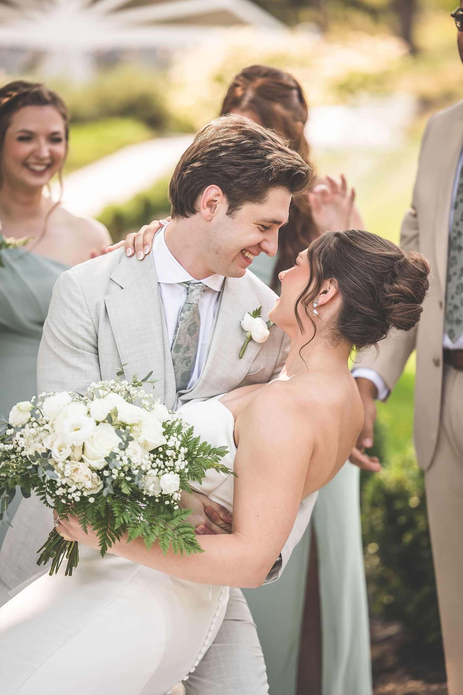Romantic wedding moment captured in natural lighting with sage green bridesmaids dresses in background.