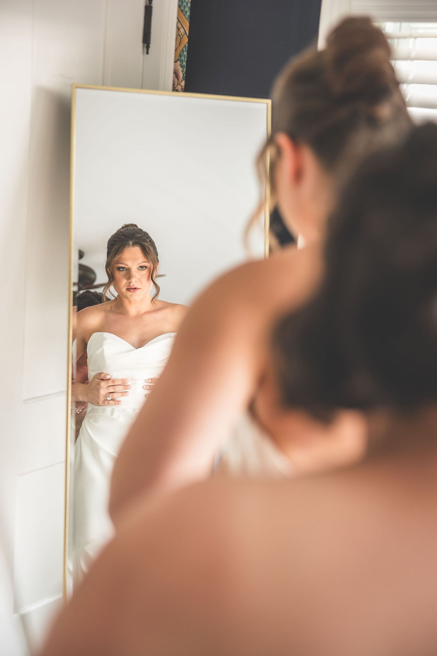 A reflection in a mirror shows someone trying on a white wedding dress while getting ready.