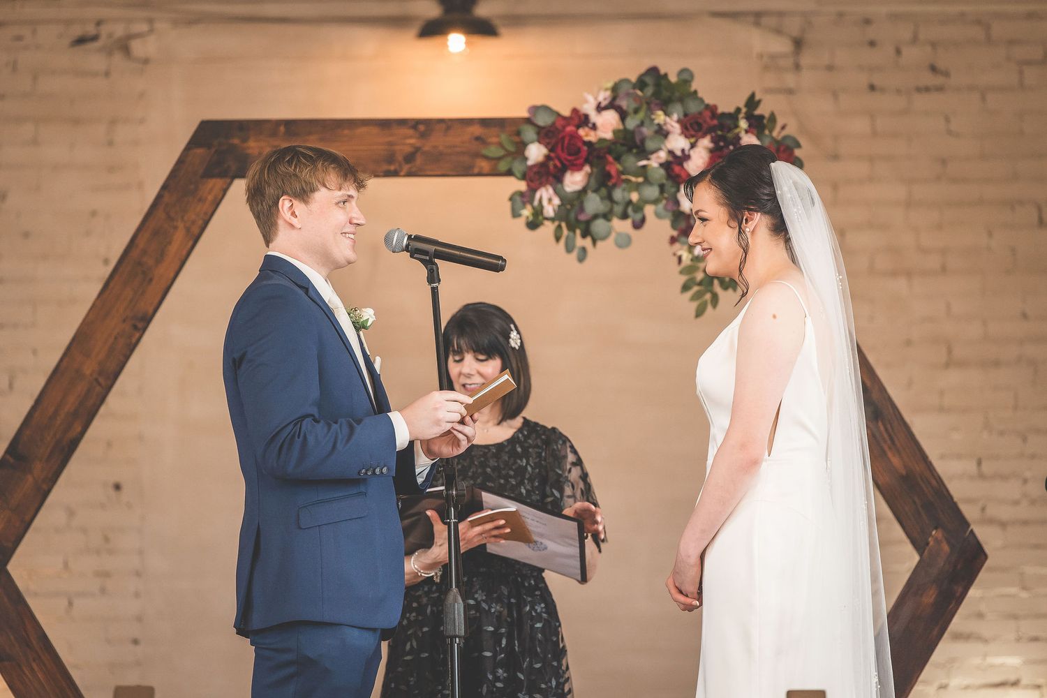 Intimate wedding ceremony scene with decorative wooden backdrop and floral accents.