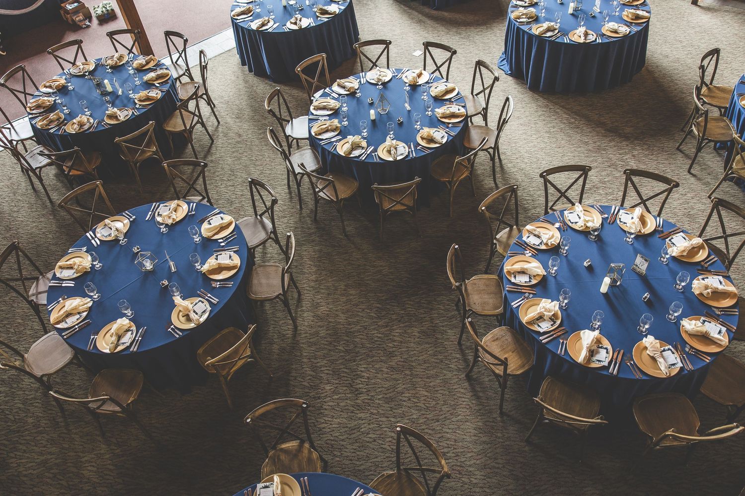 Overhead view of circular dining tables with blue tablecloths arranged for a wedding reception.