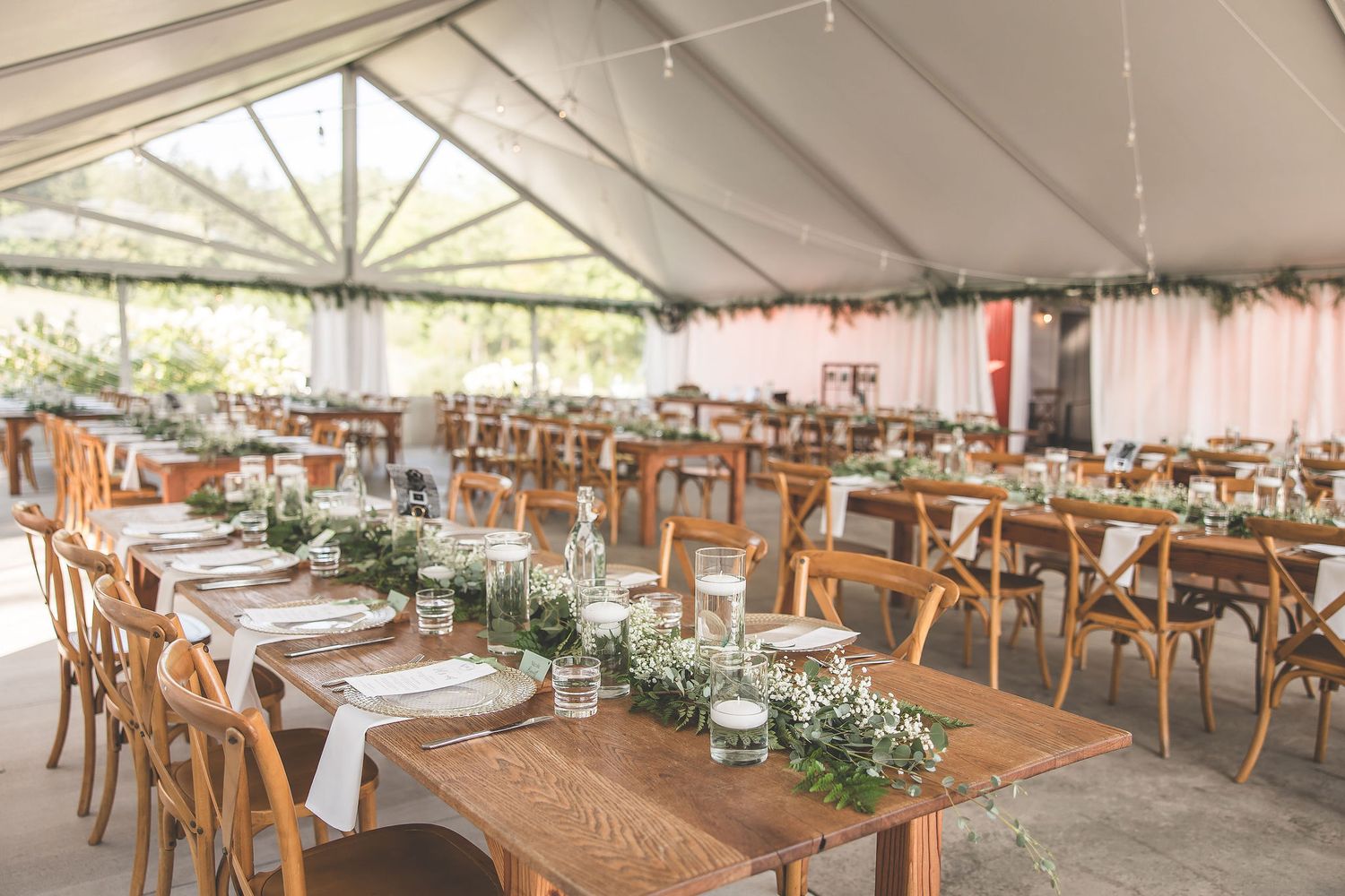 Large outdoor wedding tent setup with wooden chairs and elegant table settings.