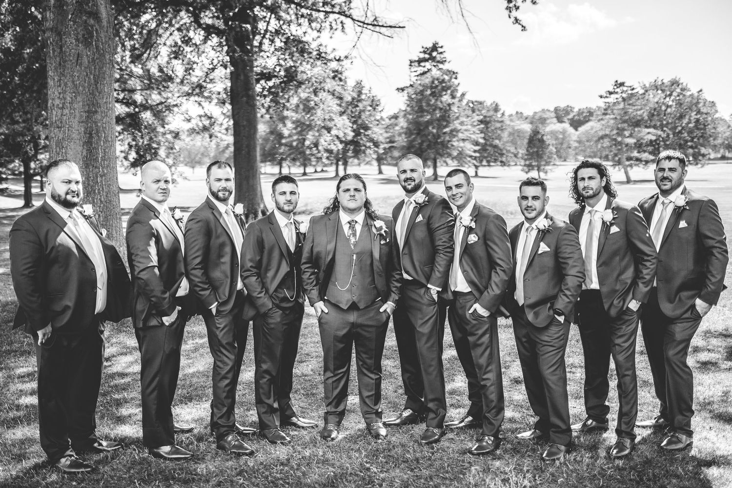Large wedding party in navy suits and sage dresses poses in a line outdoors.
