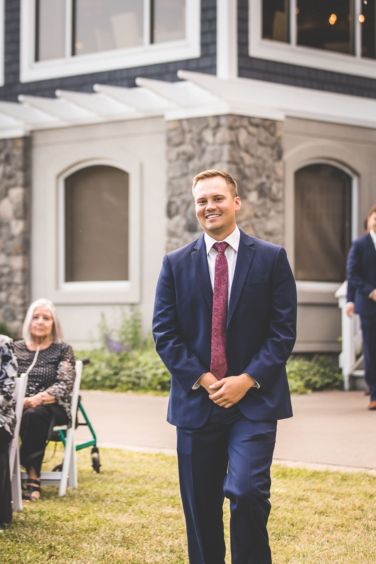 Wedding party members in navy suits and red ties standing outside a stone building.