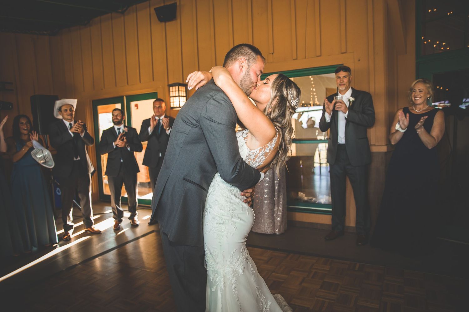 A couple shares their first dance in a rustic reception hall with wooden walls.