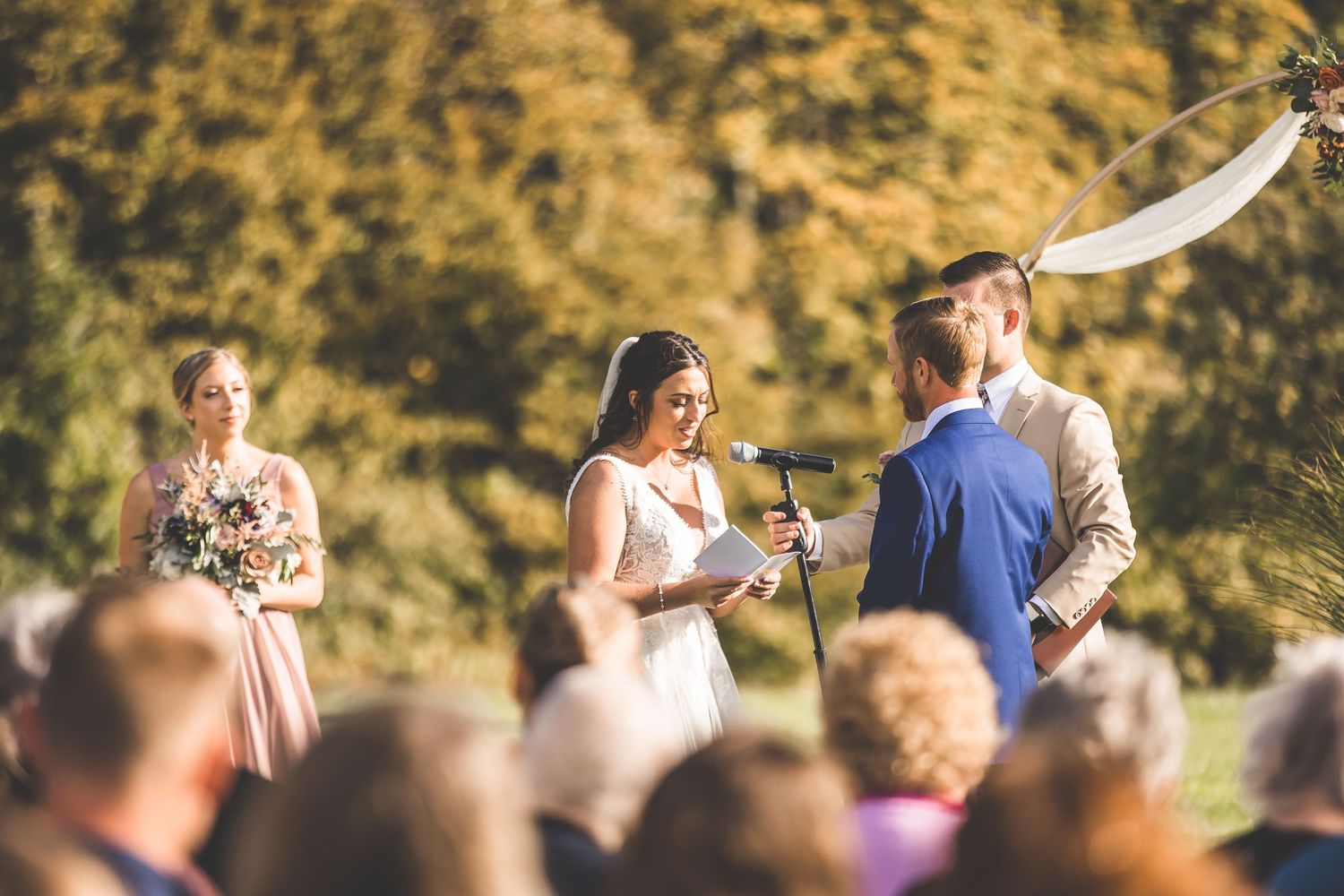 Wedding guests gather on a grassy hillside during an autumn outdoor ceremony.