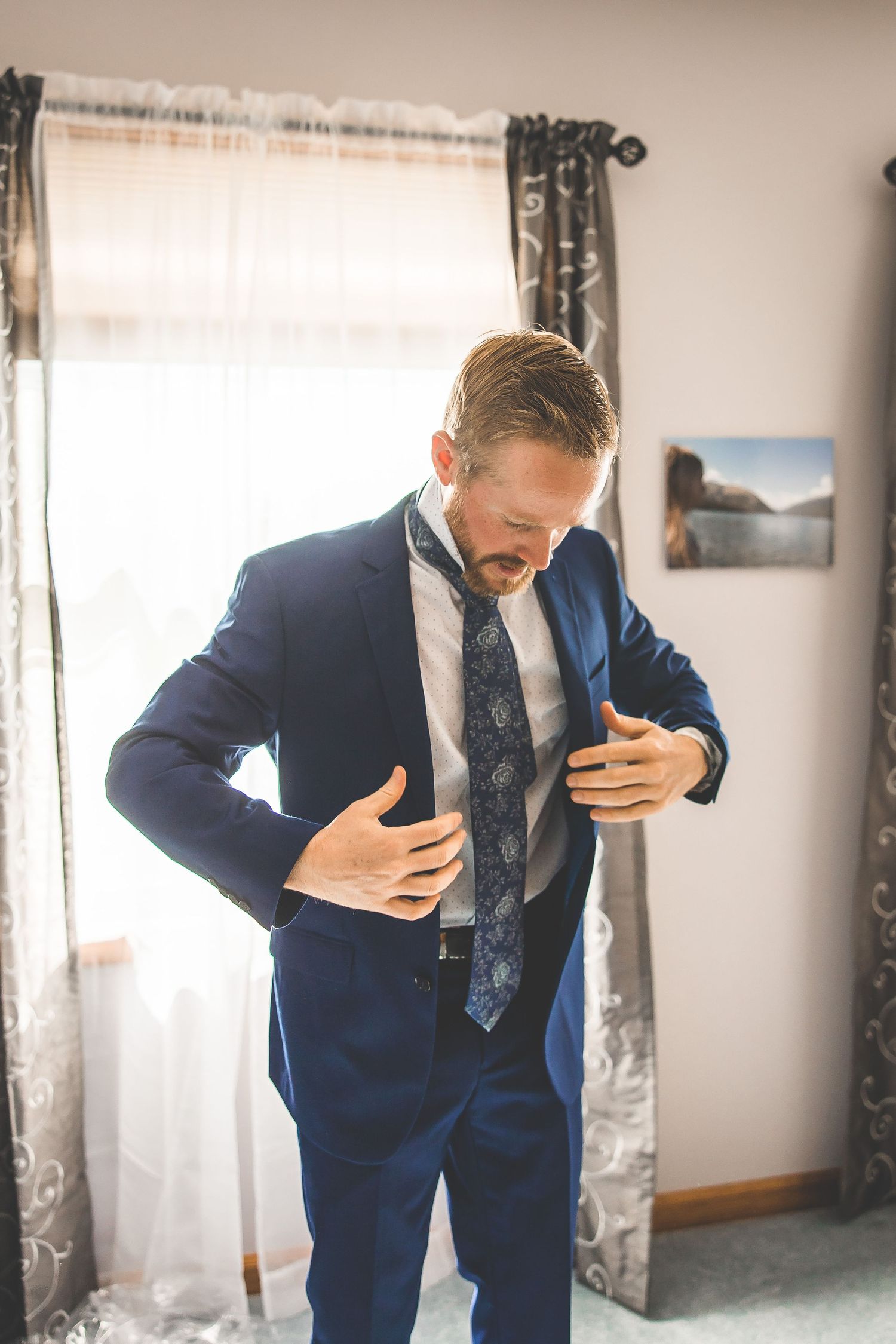 Groom in navy blue suit adjusts his tie while getting ready.