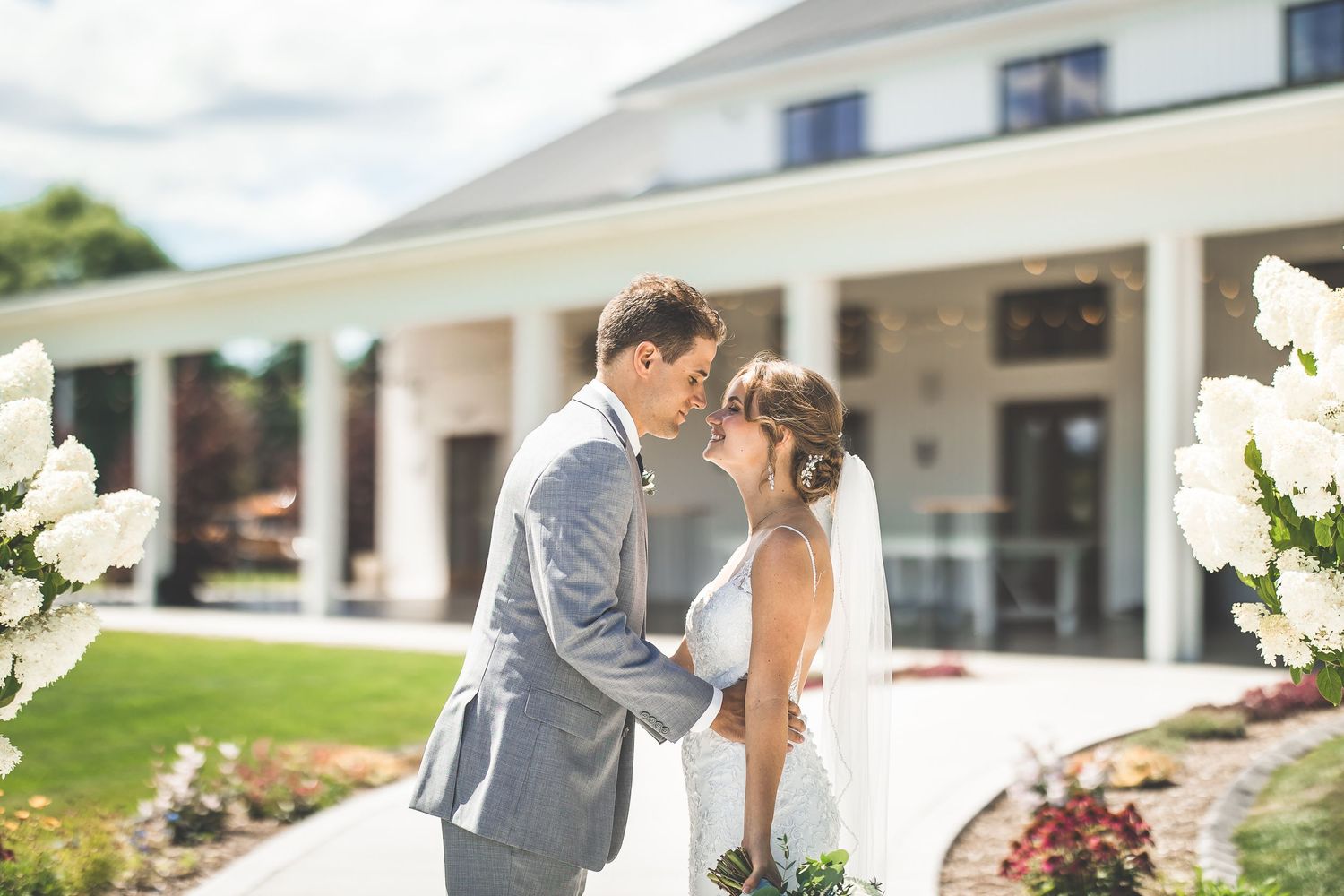 Wedding couple sharing an intimate moment outside a white building with elegant architecture.