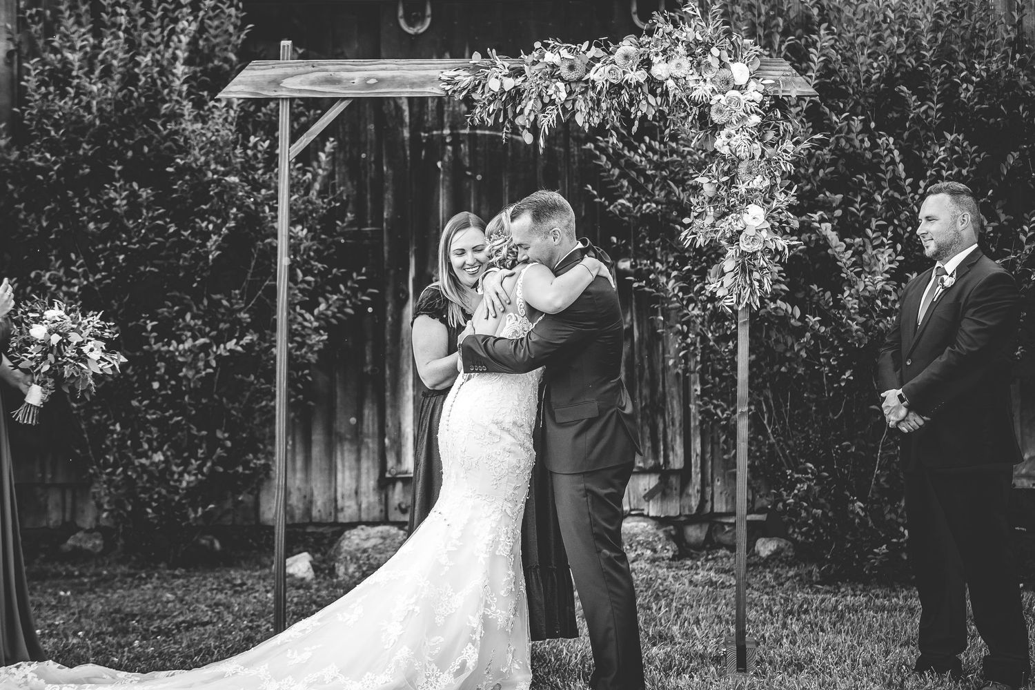 Black and white capture of wedding ceremony moments under rustic wooden arch.