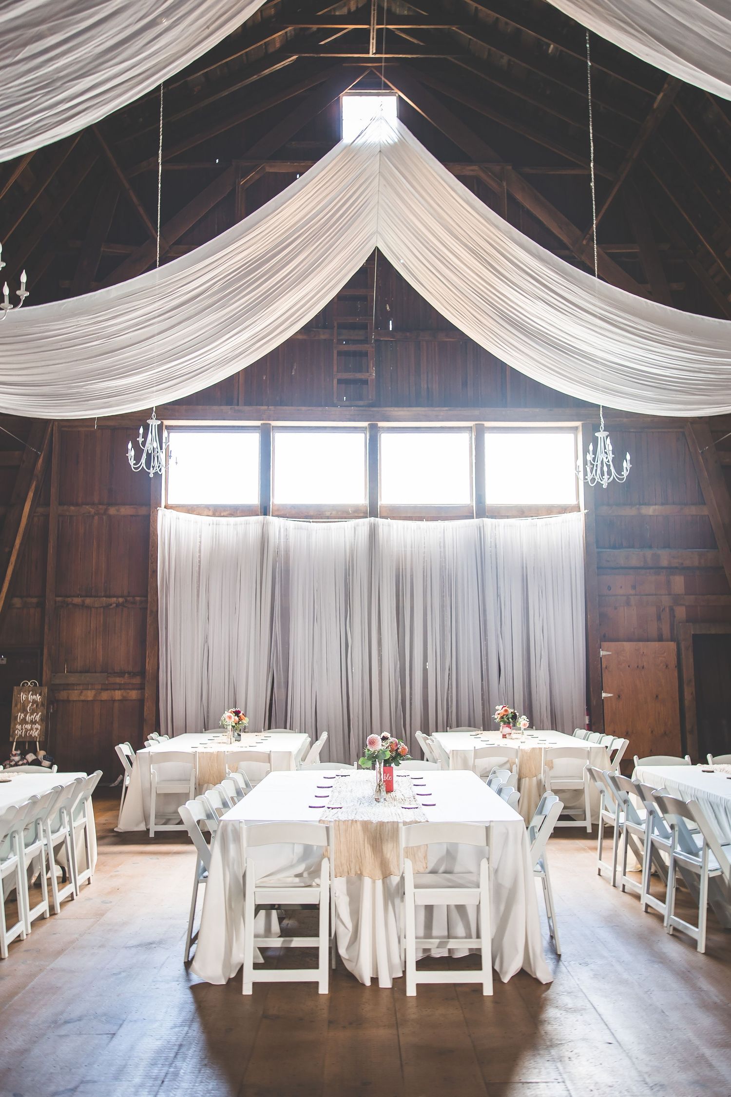 Elegant barn wedding reception setup with white draping and chandeliers.