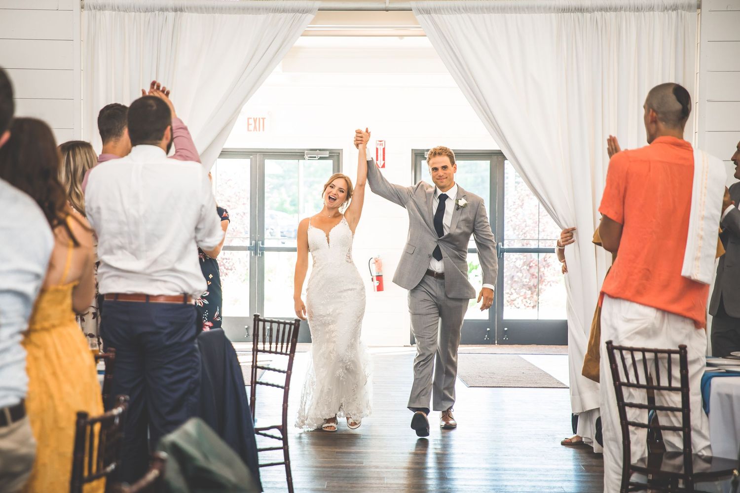Wedding guests dance together in an elegant reception venue with white decor and hardwood floors.