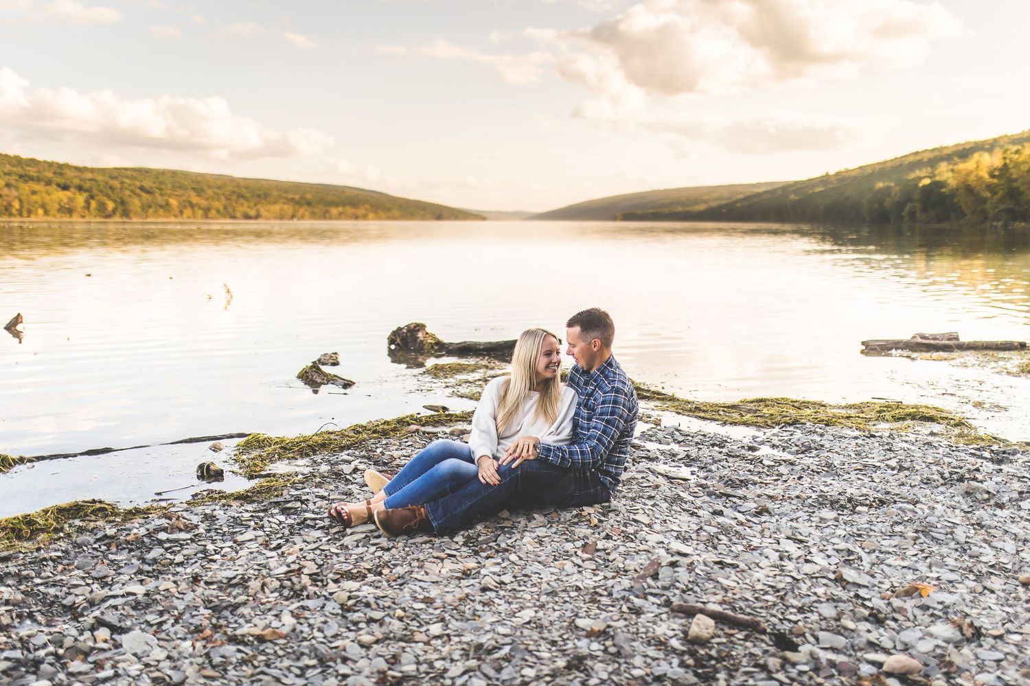 Couple enjoying a romantic sunset on a rocky beach with mountains in the background.