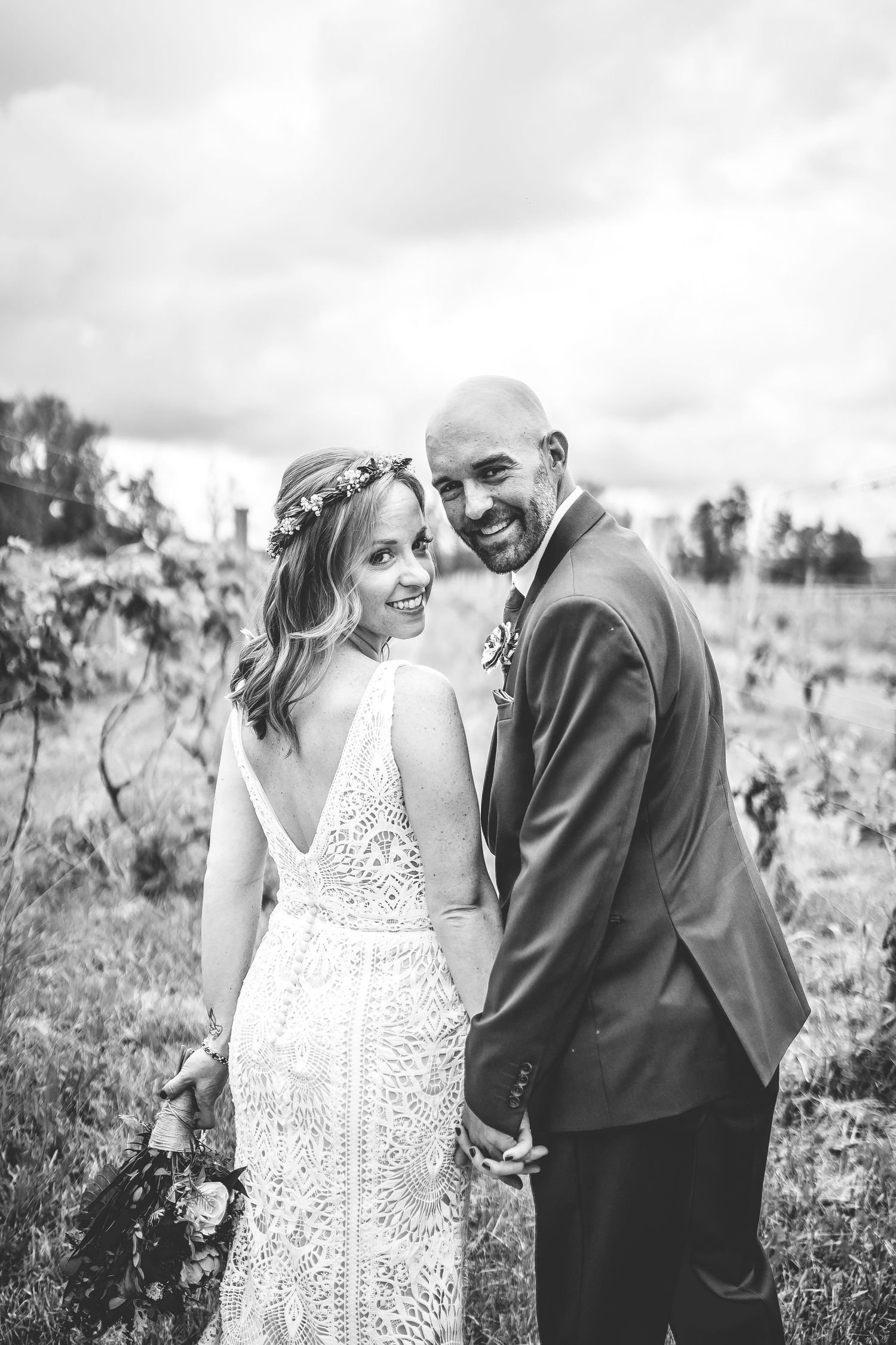 Elegant couple shares laughter during their wedding photoshoot in a rustic vineyard setting.