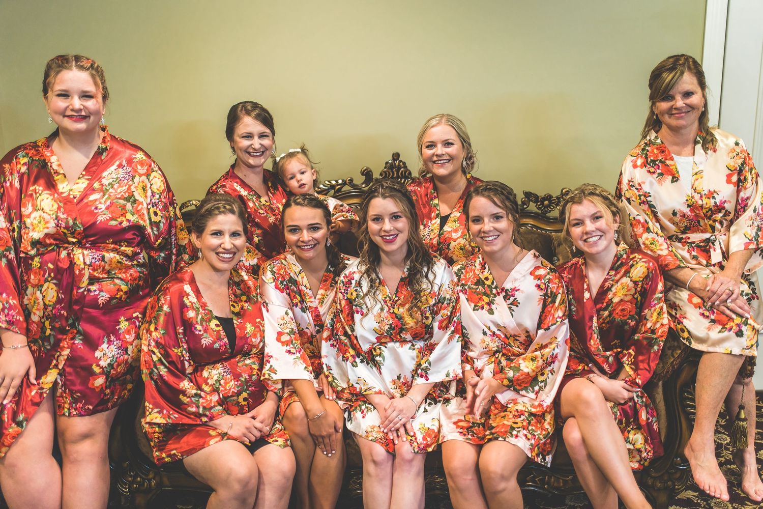Group wearing matching floral robes sitting together on a couch during wedding preparations.