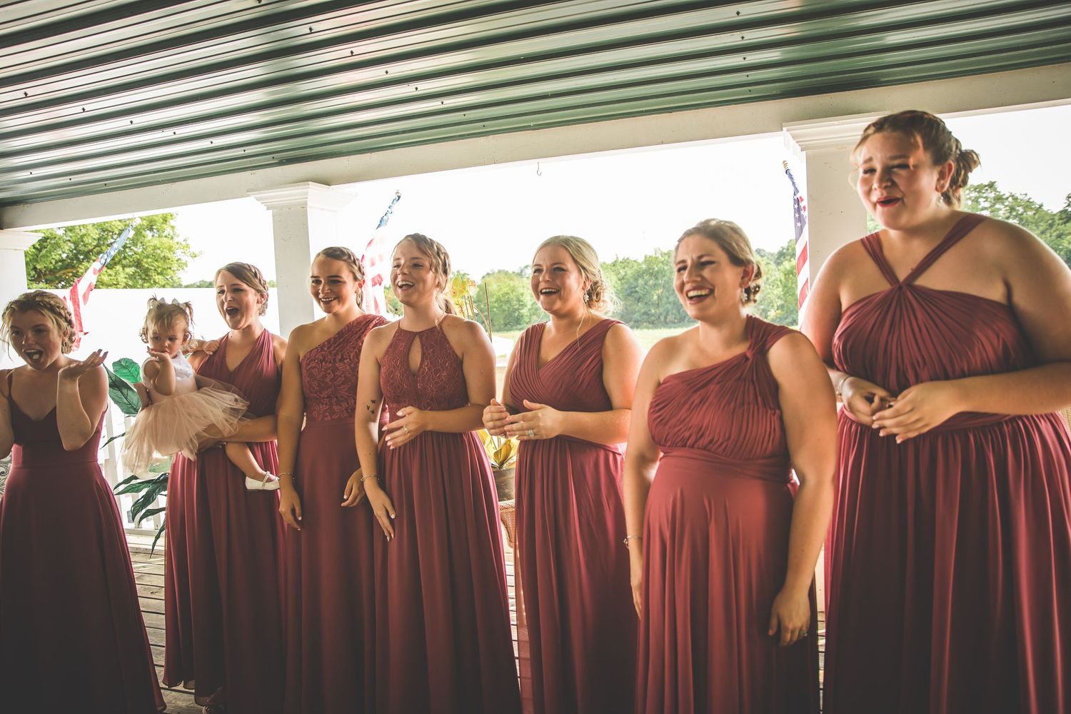 Line of bridesmaids in matching burgundy dresses posing for a group photo.