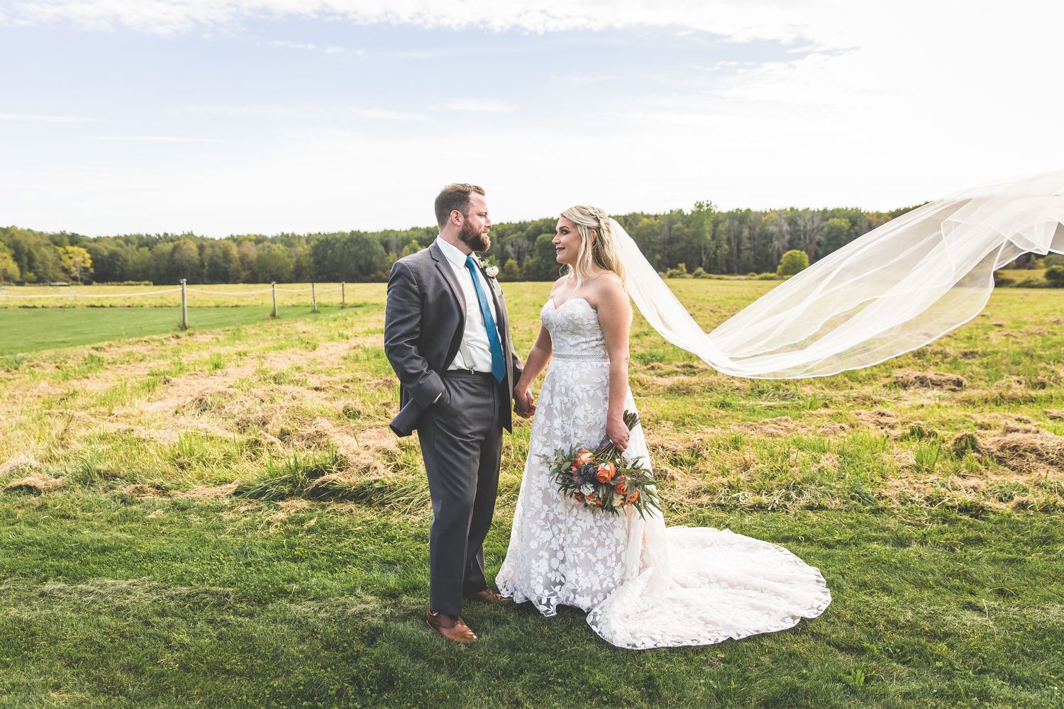 Wedding party walking across scenic field with mountains and forest in background.