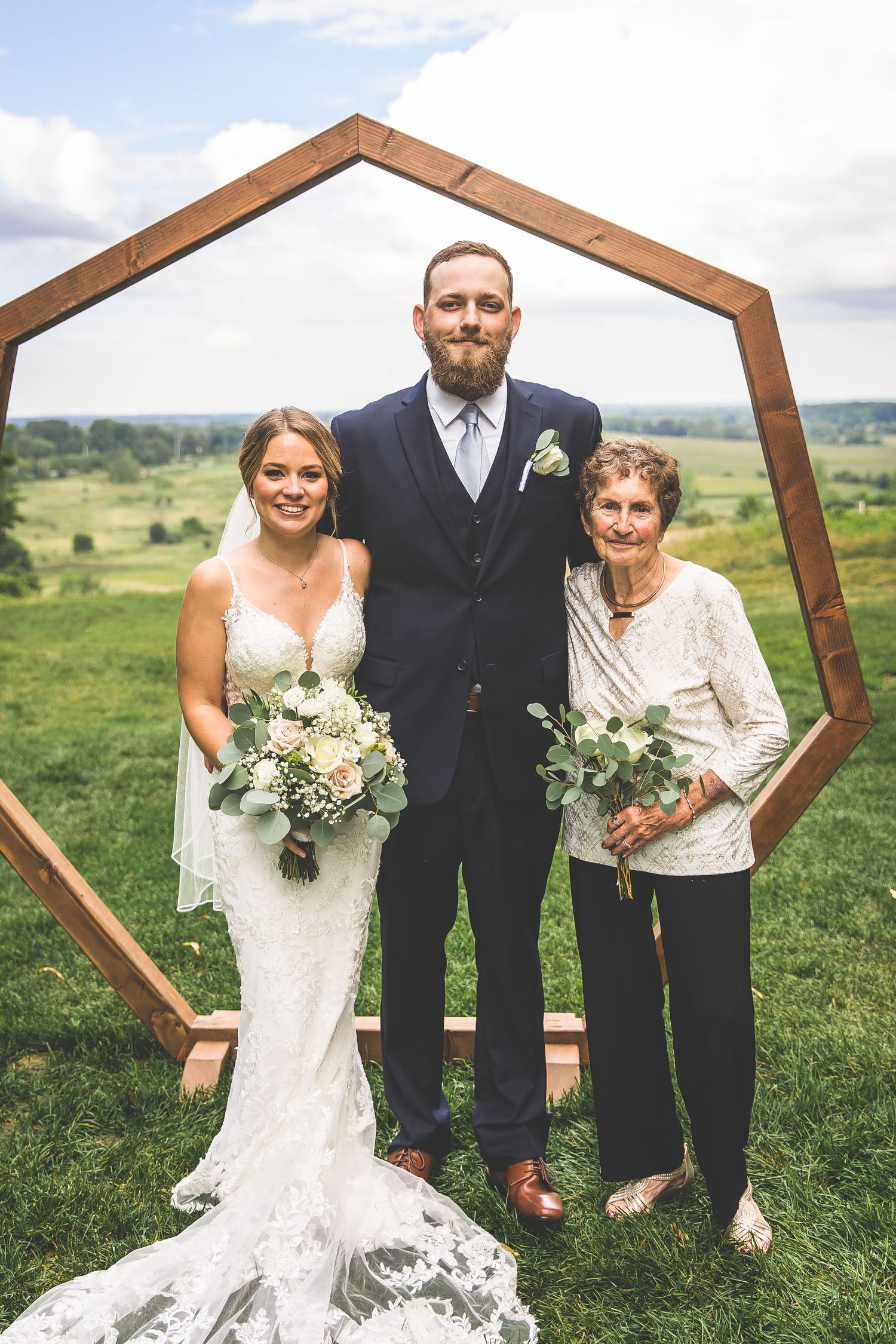 Wedding portrait under wooden hexagonal arch with scenic countryside backdrop.