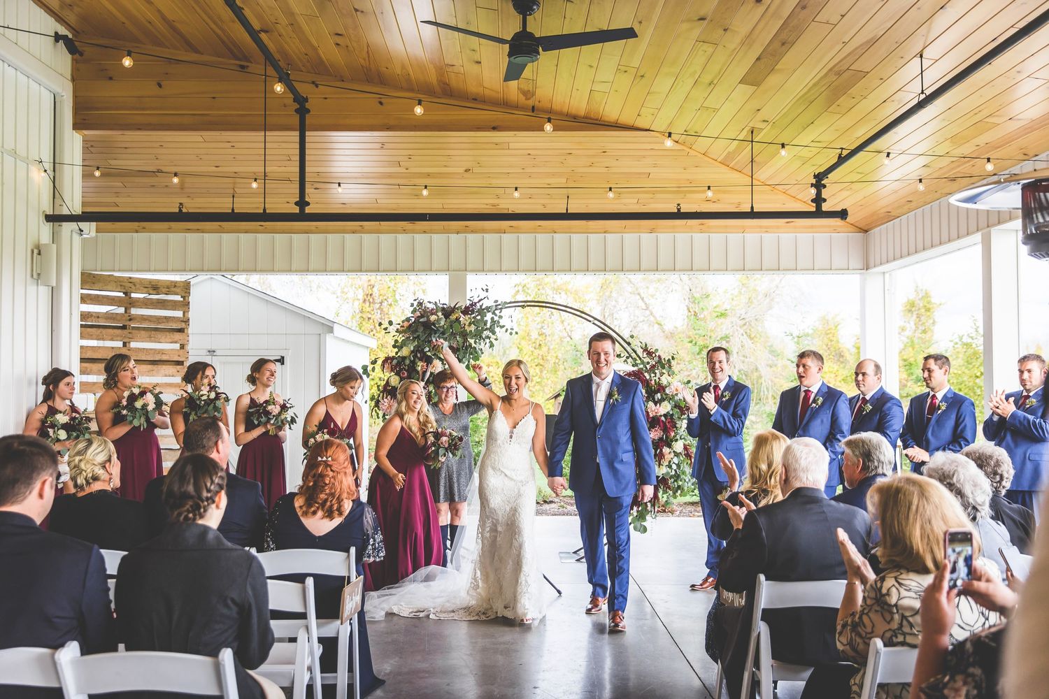 Indoor wedding ceremony in modern venue with wooden ceiling and string lights creating warm ambiance.