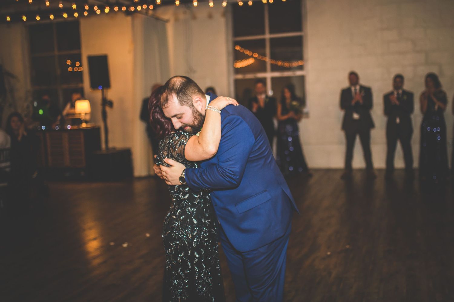 Wedding reception venue with string lights and guests dancing on wooden floor.