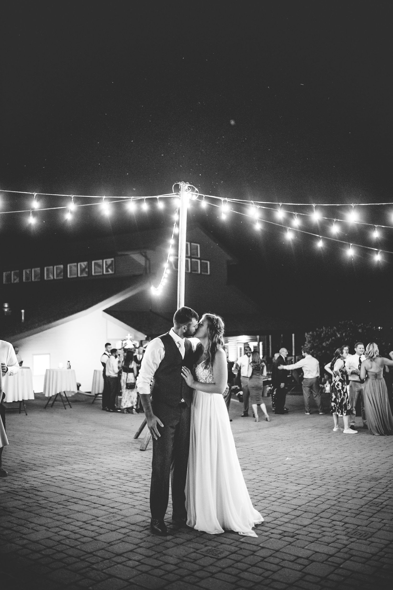 String lights illuminate a brick patio during an evening wedding reception.