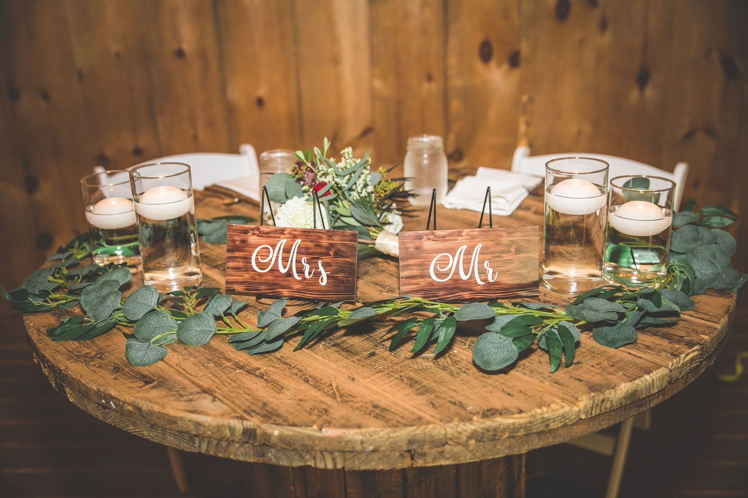 Rustic wooden table decorated with greenery and mason jars for wedding reception.