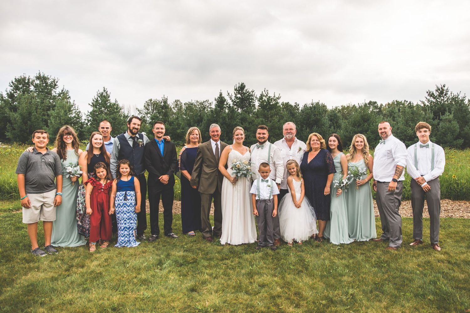 Large wedding party group poses for formal photos in an outdoor rustic setting.