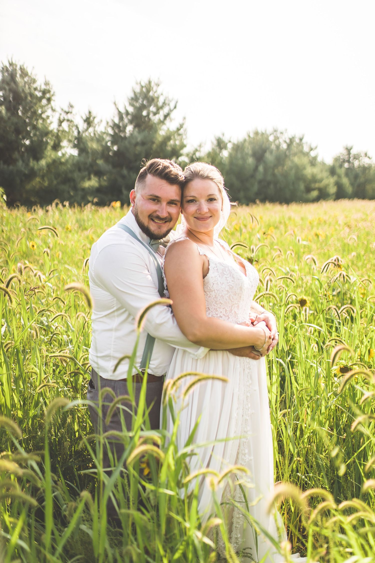 Newlywed couple embraces in a sun-lit field of tall grass.