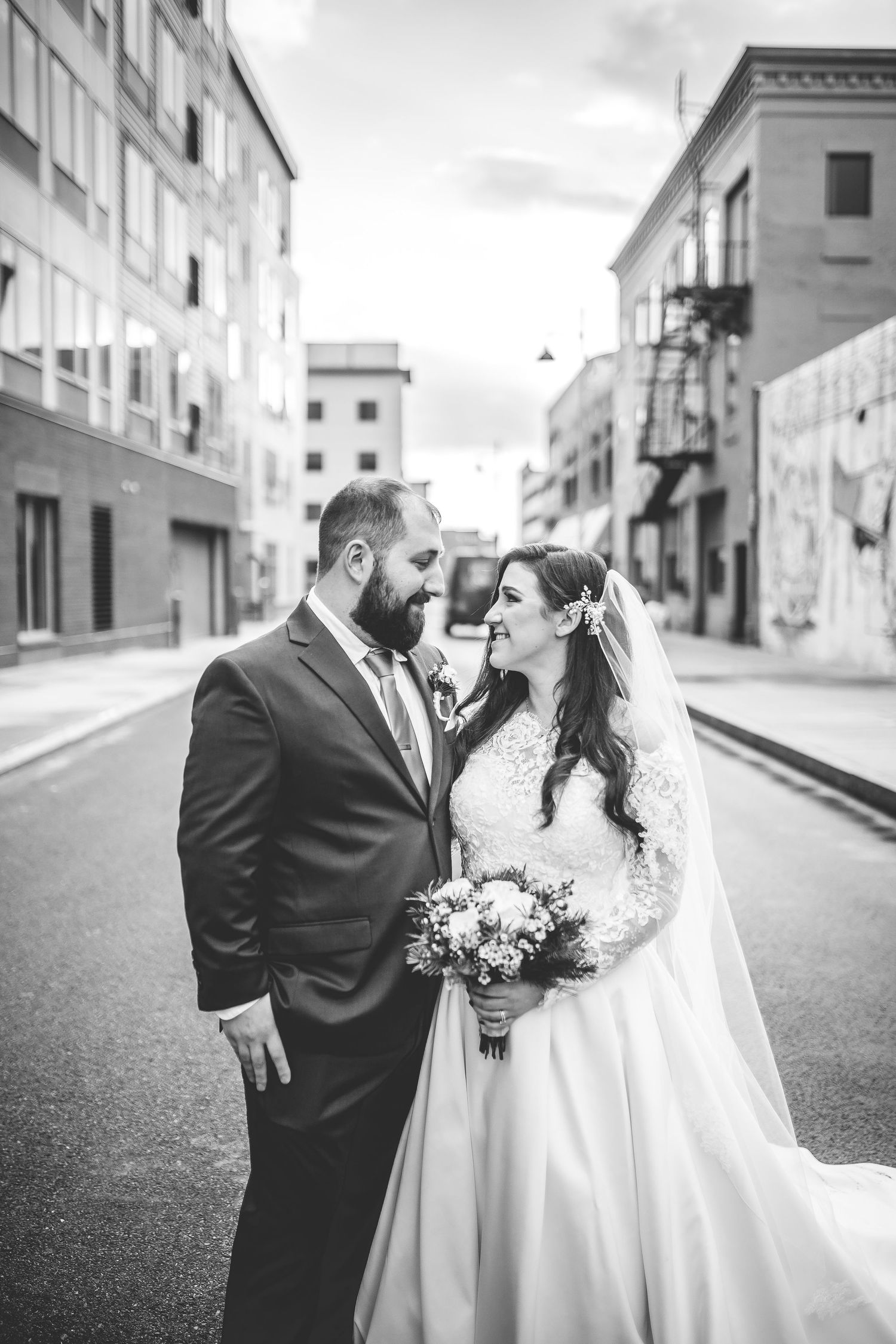 Black and white portrait of newlyweds sharing intimate moment on urban street.