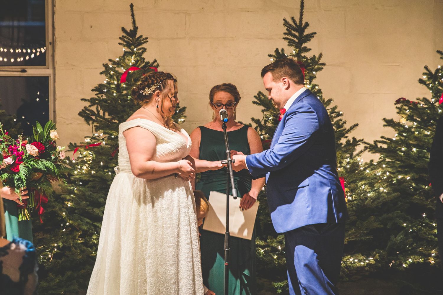 A wedding ceremony takes place in front of decorated Christmas trees with guests watching.
