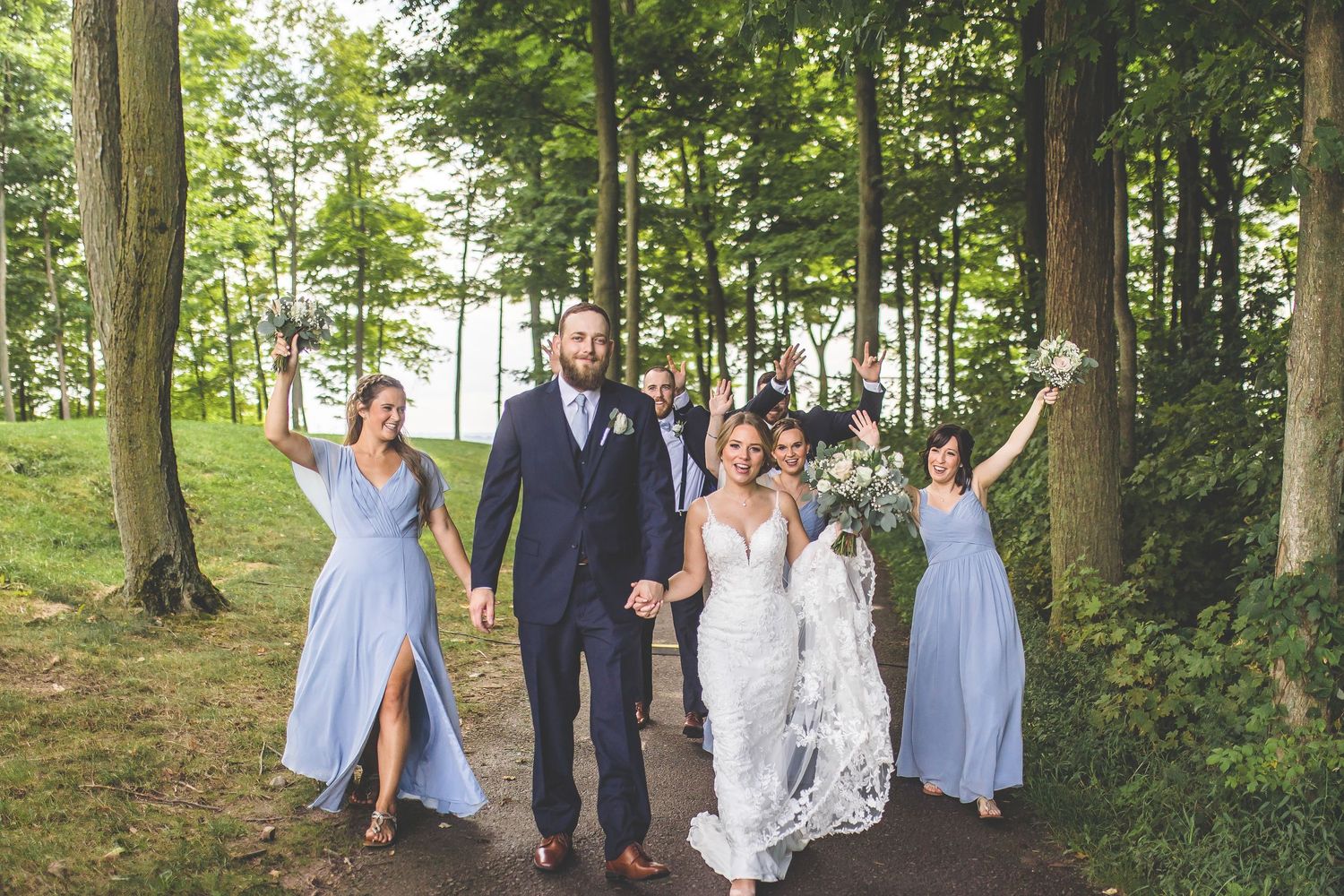 Wedding party walks through wooded area with bridesmaids in light blue dresses.