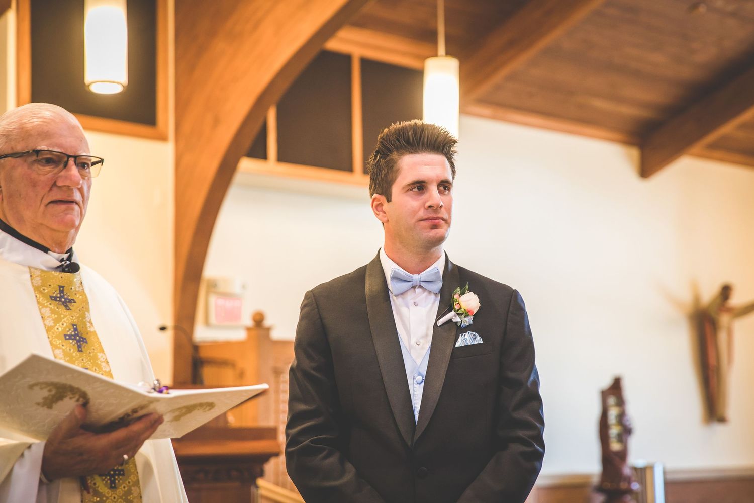 Church interior with exposed wooden beams and pendant lighting during a wedding ceremony.