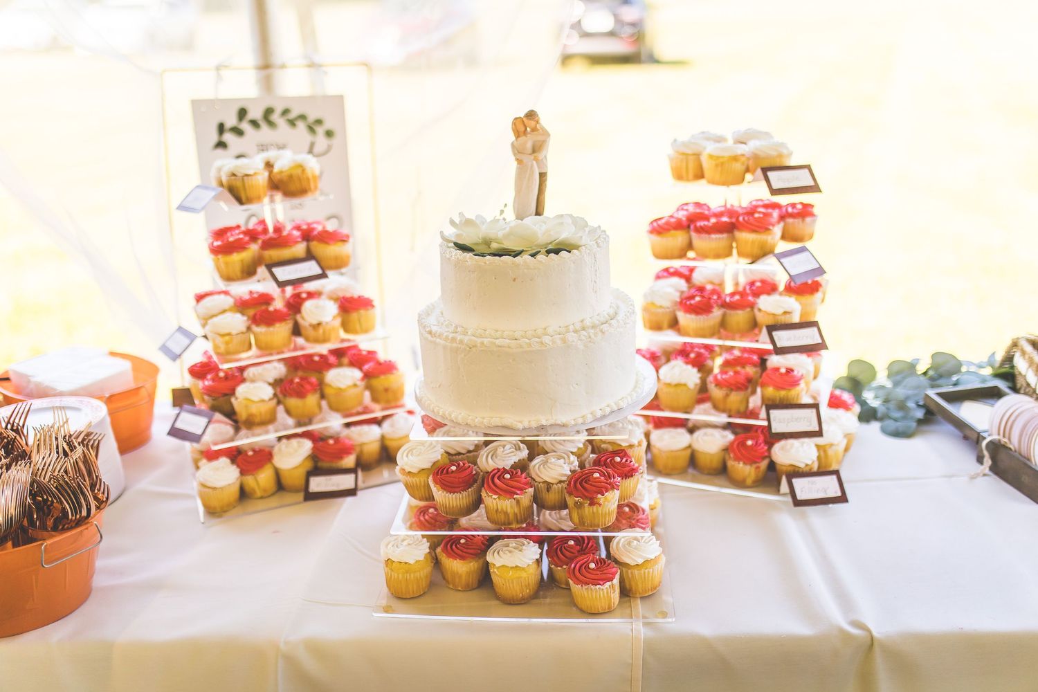 Wedding dessert display featuring white cake and colorful cupcakes on tiered stands.