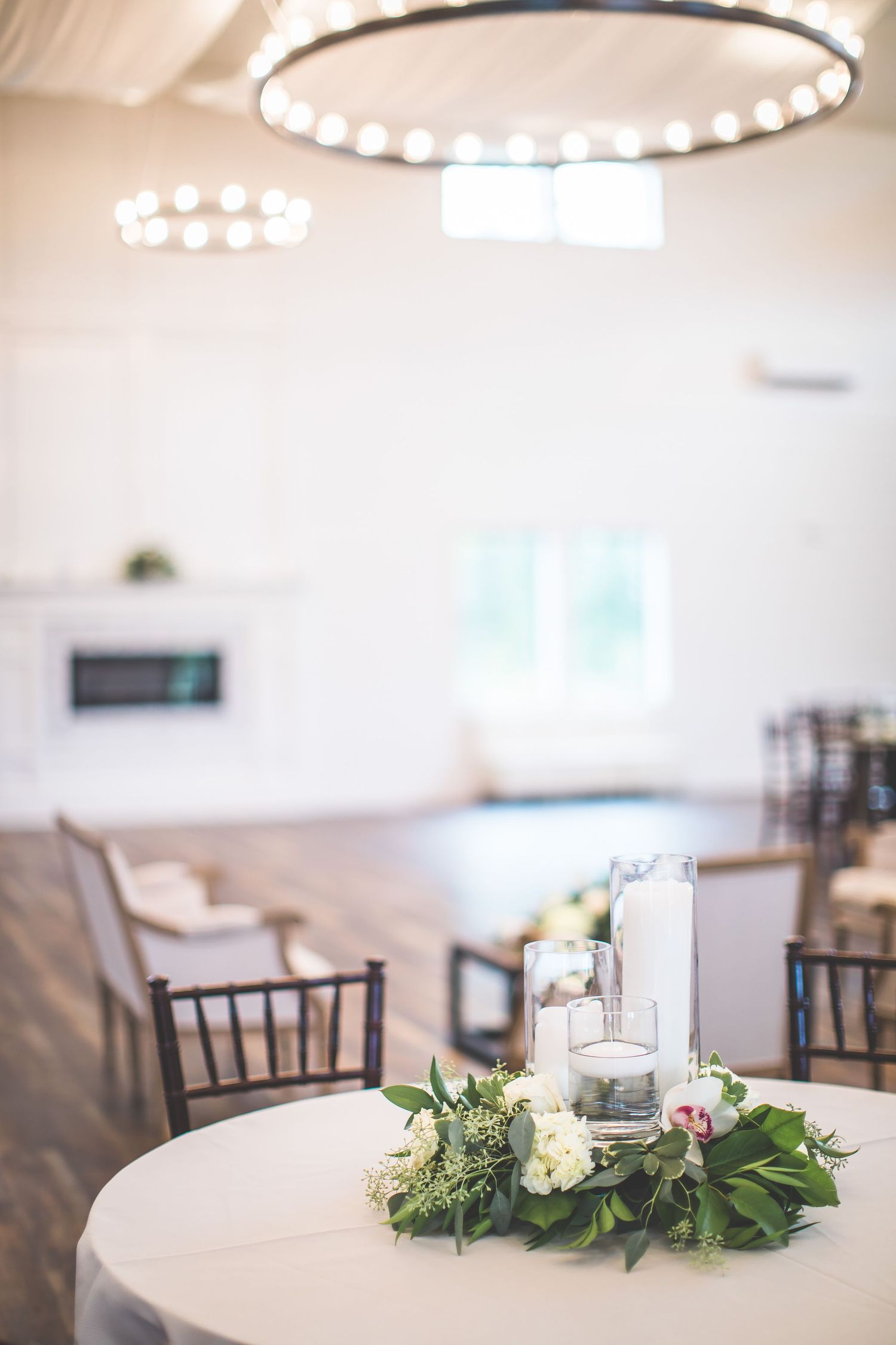 Elegant wedding reception tables with simple greenery centerpieces and string lights overhead.